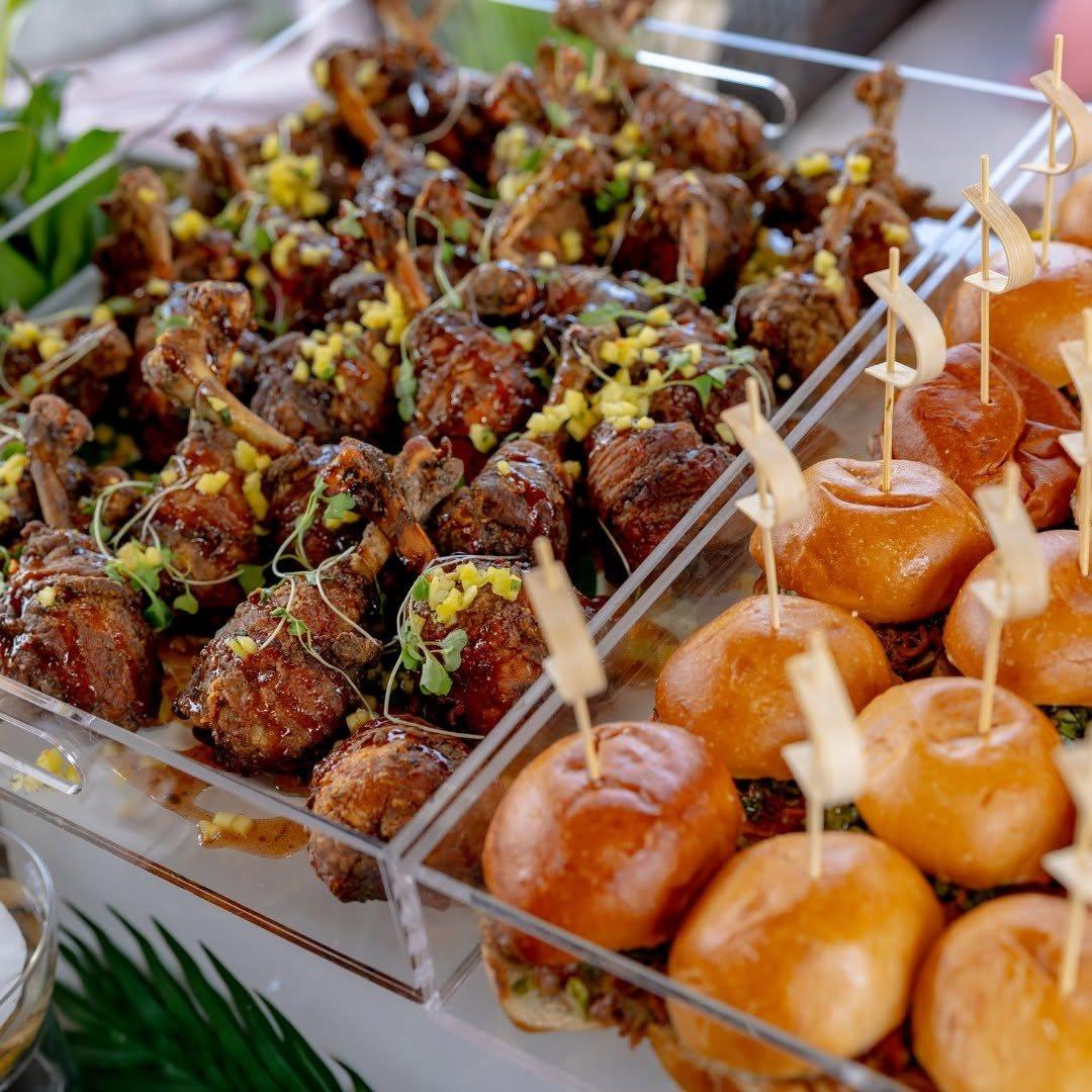 Glazed chicken lollipops beside sliders on an acrylic display